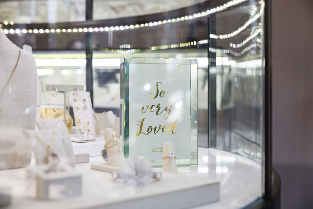 Glass sign that says "So Very Loved"